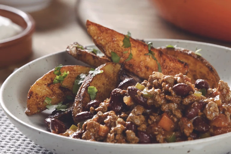 A bowl of Quorn Mince and kidney bean chilli with potato wedges on the side.