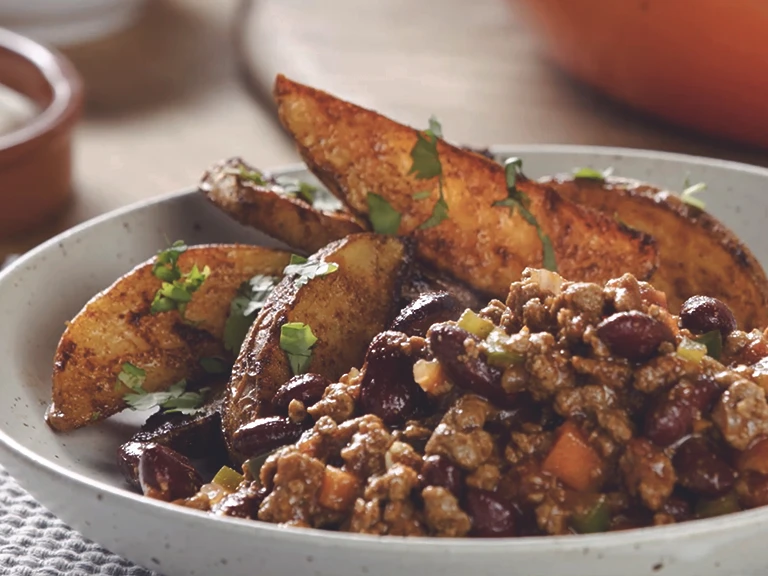 A bowl of Quorn Mince and kidney bean chilli with potato wedges on the side.