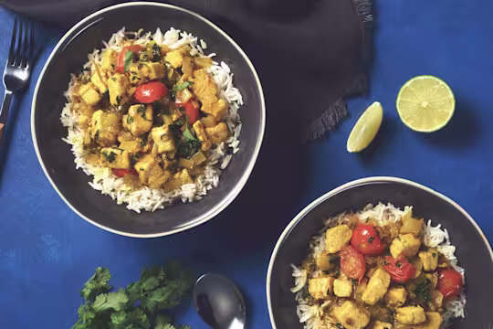 Two bowls of rice and brazilian coconut curry with Quorn Pieces sat beside two wedges of lime.