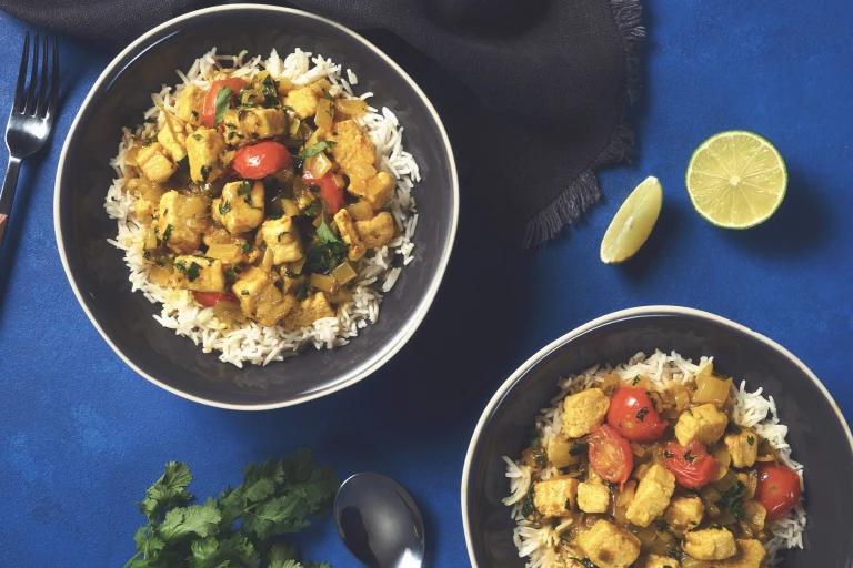 A Brazilian curry with Quorn Pieces and cherry tomatoes in a coconut sauce atop a bed of white rice with half a lime on the side for serving.