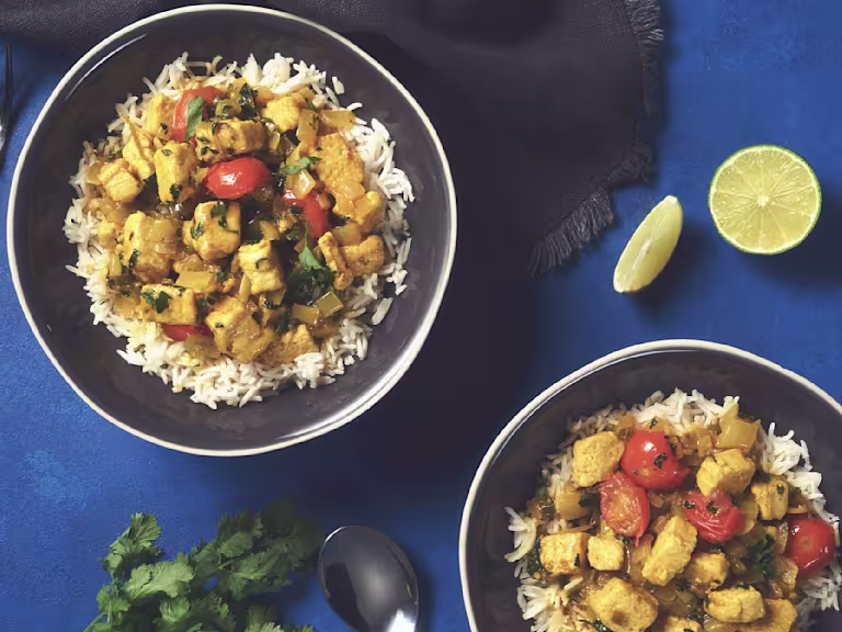 Two bowls of rice and brazilian coconut curry with Quorn Pieces sat beside two wedges of lime.