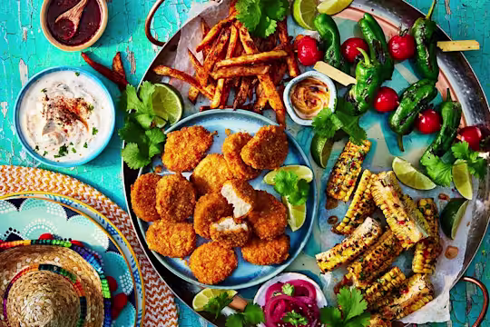 Quorn Cheesy Nacho Nuggs on a sharing platter with corn on the cob, chips, and tomato and lettuce skewers. Small sombrero and dips to the side.