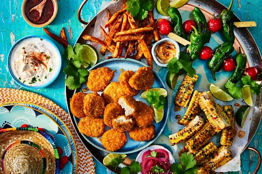 Quorn Cheesy Nacho Nuggs on a sharing platter with corn on the cob, chips, and tomato and lettuce skewers. Small sombrero and dips to the side.