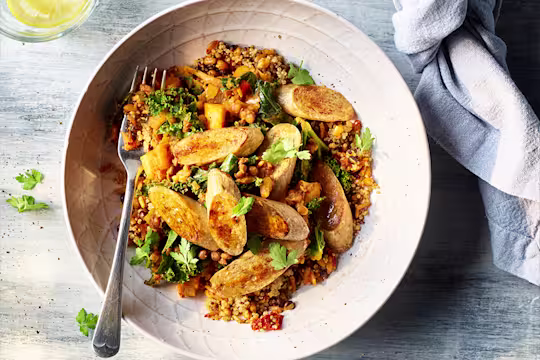 Pearl barley, Quorn sausages and winter lentils served in a round bowl with lemon water on the side.