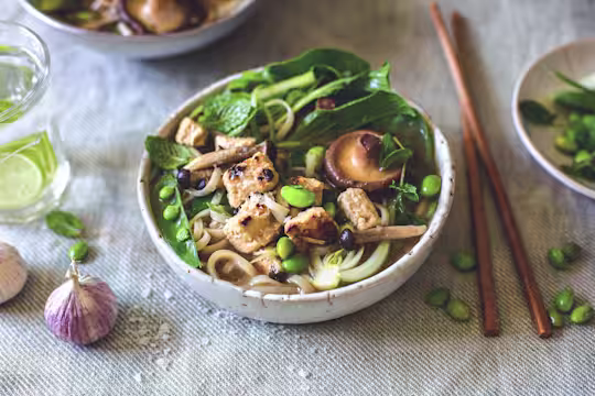 An udon noodle soup topped with mushrooms, pak choi, peas, edamame, and Quorn Pieces.