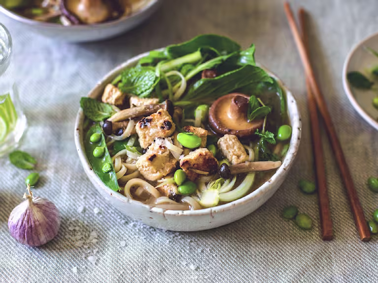An udon noodle soup topped with mushrooms, pak choi, peas, edamame, and Quorn Pieces.