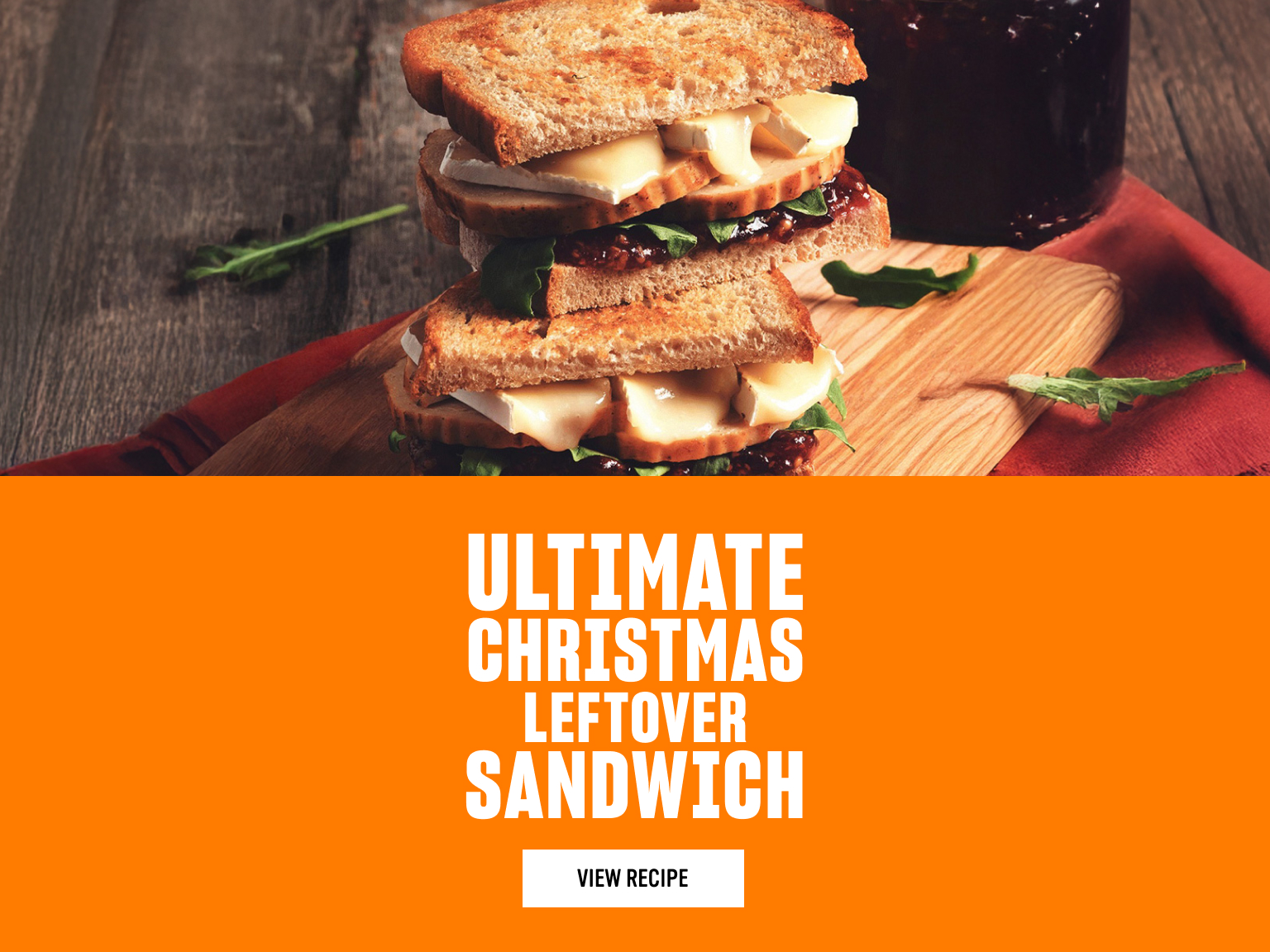 Boxing day sandwich with turkey slices, melted brie, greens, and cranberry sauce on a wooden board, beside an orange panel featuring white text reading “Ultimate Christmas Leftover Sandwich” with a “View Recipe” button.