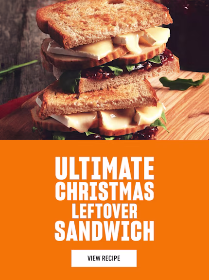 Boxing day sandwich with turkey slices, melted brie, greens, and cranberry sauce on a wooden board, beside an orange panel featuring white text reading “Ultimate Christmas Leftover Sandwich” with a “View Recipe” button.