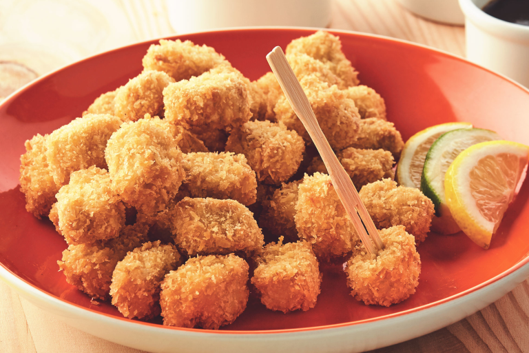 A plate piled high with breaded popcorn bites made with Quorn Pieces with citrus wedges on the side for serving.