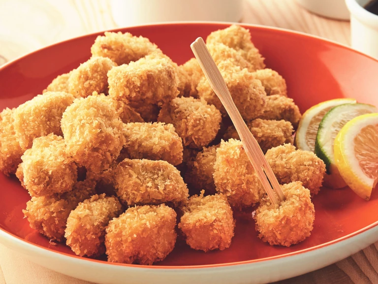 A plate piled high with breaded popcorn bites made with Quorn Pieces with citrus wedges on the side for serving.