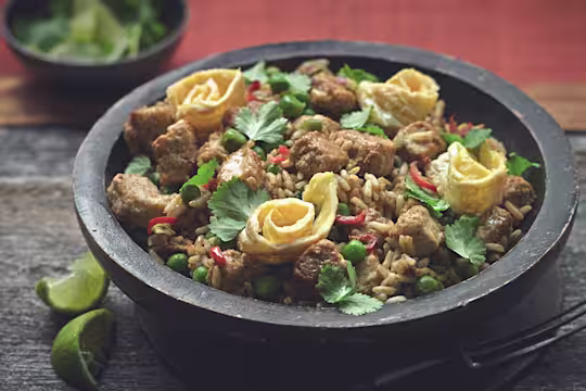 Rice dish of Nasi Goreng made with Quorn Pieces, served in a bowl topped with chilli, coriander and omelette rolls