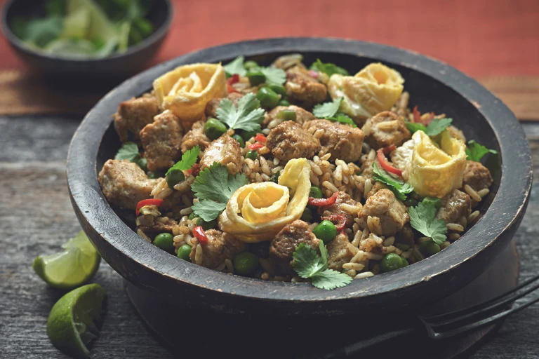 Rice dish of Nasi Goreng made with Quorn Pieces, served in a bowl topped with chilli, coriander and omelette rolls