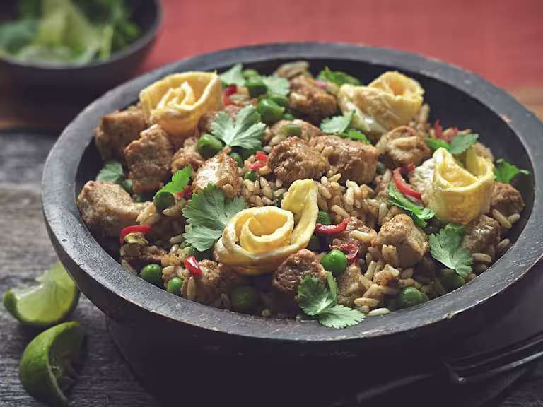 Rice dish of Nasi Goreng made with Quorn Pieces, served in a bowl topped with chilli, coriander and omelette rolls