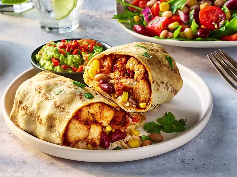 Air fryer vegetarian burrito cut in half to show the filling including Quorn Pieces, sweetcorn and kidney beans with a side of guacamole.