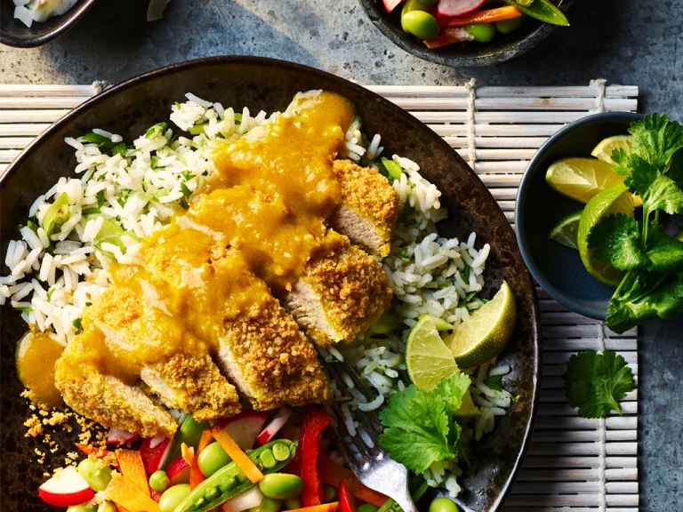 Quorn Vegan Katsu Fillets topped with katsu curry sauce served on a bed of lime and coriander rice. Various vegetables on the side with a side dish of lime and coriander.