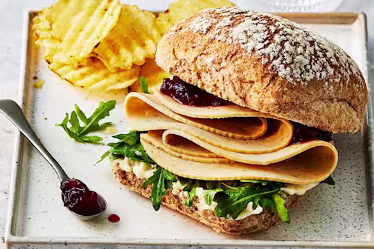 Quorn turkey slices in a sandwich with rocket leaves and cranberry sauce with crisps on a tray