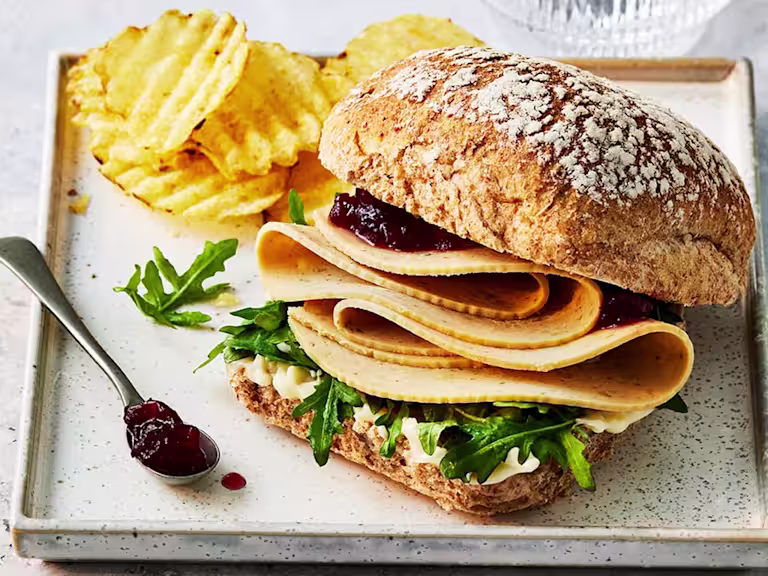 Quorn turkey slices in a sandwich with rocket leaves and cranberry sauce with crisps on a tray