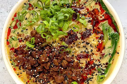 Quorn mince in a white bowl of Tantan-style broth with noodles, bok choy and spring onion garnish.