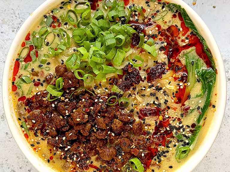 Quorn mince in a white bowl of Tantan-style broth with noodles, bok choy and spring onion garnish.