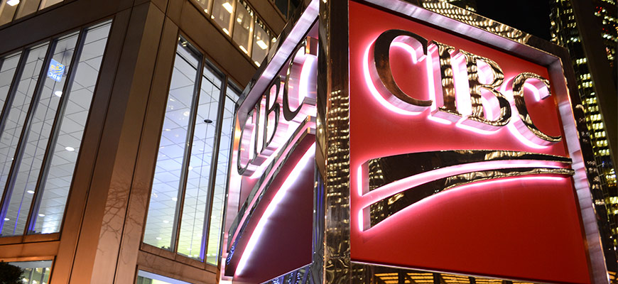 This photo is of the CIBC logo outside of the building. The CIBC logo is red and yellow and lit up in the dark. 
