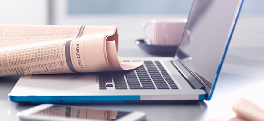 A newspaper resting on a new computer. A phone and coffee cup are in the shot as well. 