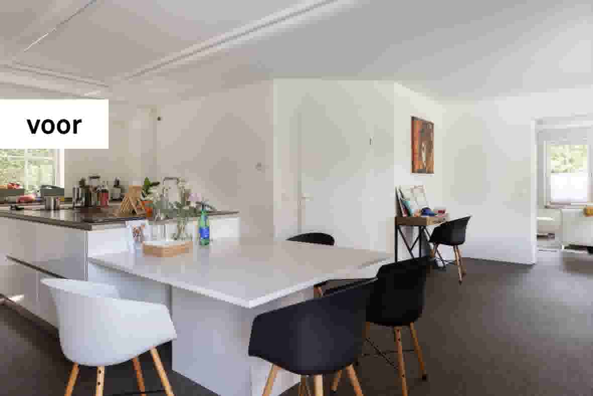 Moderne open keuken met wit kookeiland, zwarte en witte stoelen, en aangrenzende eetkamer met kunstwerk aan de muur.