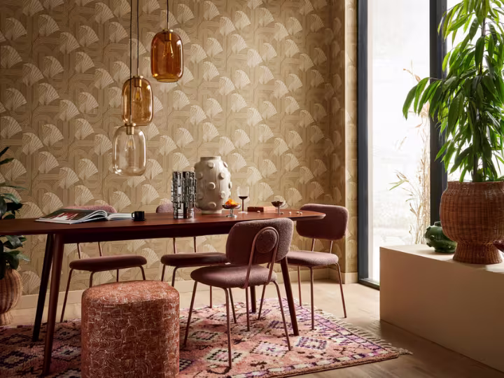 Modern eetkamer met bruine stoelen, houten tafel, amberkleurige hanglampen, beige behang met waaierpatroon en groene plant.