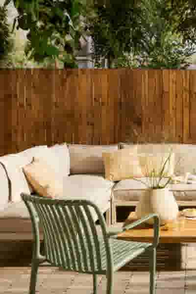 Gezellige buitenruimte met beige loungebank, groene stoel en houten schutting, perfect voor ontspanning in de tuin.
