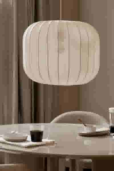 Moderne witte lampenkap boven een eettafel met koffiekopje en bord in een stijlvol interieur met beige tinten.