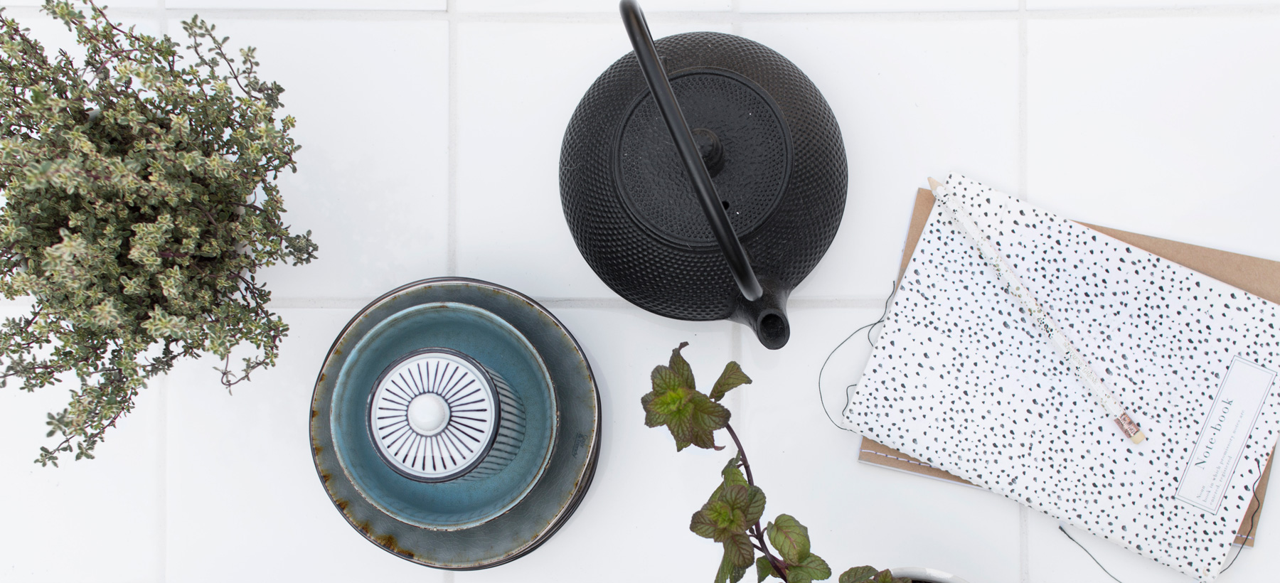 Betegelde tafel met servies, planten en een schrift van bovenaf gezien
