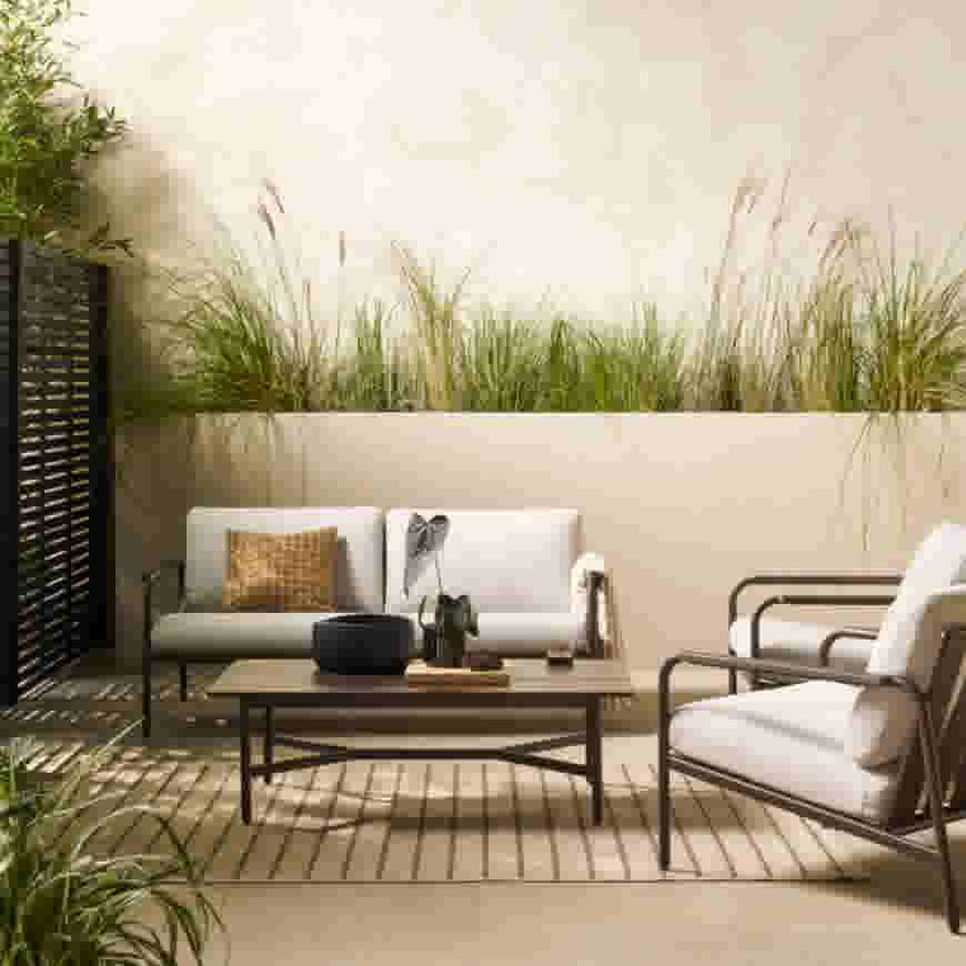 Modern terras met witte loungemeubels, houten salontafel en decoratieve siergras in beige plantenbakken tegen lichte muur.