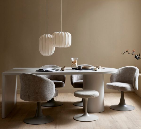 Moderne eetkamer met witte hangende lampen, ovale tafel, grijze stoelen en een koffieset in een minimalistische beige ruimte.