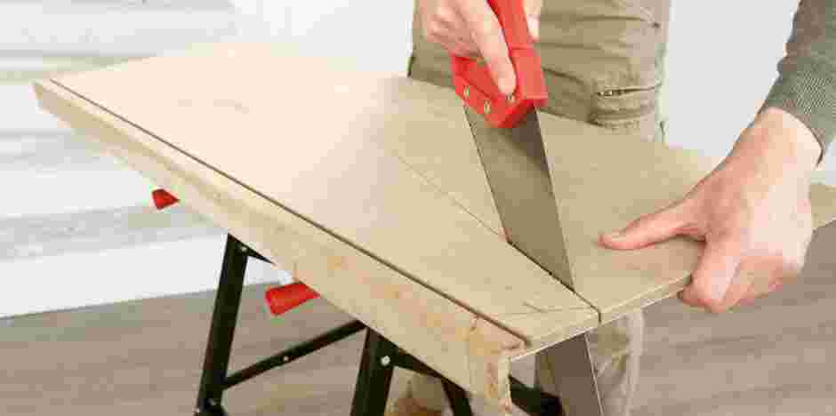 Persoon zaagt houten plank met rode handzaag op werkbank in witte werkruimte.