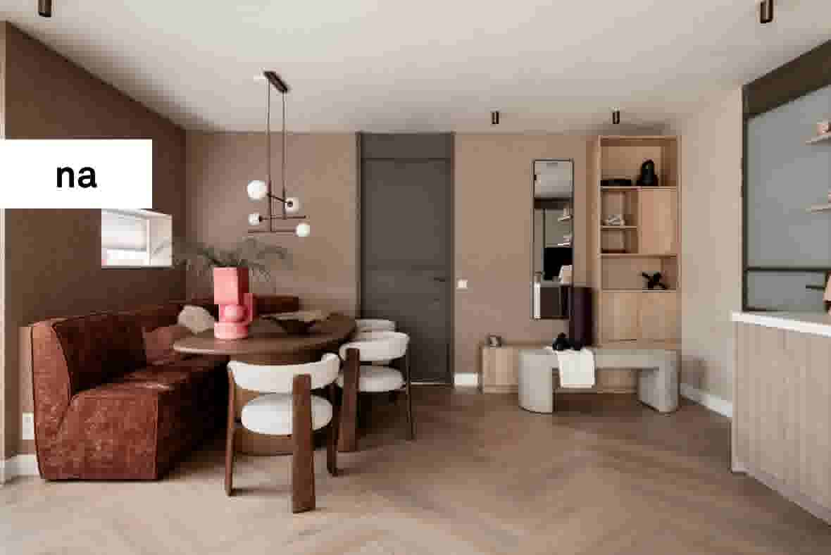 Modern interieur met roze en bruine tinten, ronde eettafel, fluwelen bank, houten kast en designverlichting.