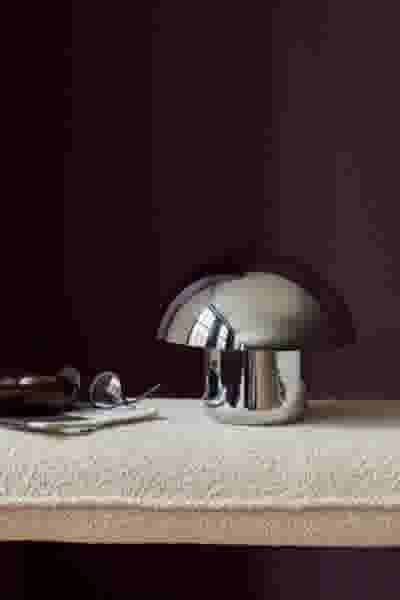 Glanzende paddenstoelvormige metalen lamp op een lichte stoffen ondergrond tegen een donkere paarse muur.
