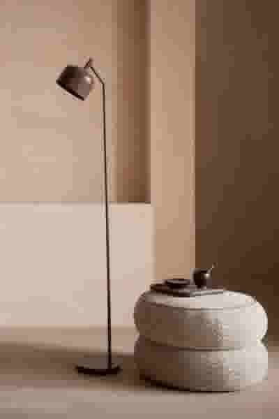 Moderne staande lamp naast een ronde gestapelde poef in een minimalistische beige kamer met rustgevende sfeer.