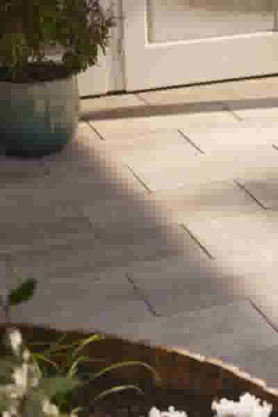 Grijze betontegels op een terras bij een witte deur, met een blauwe plantenpot en bloemen op de voorgrond.