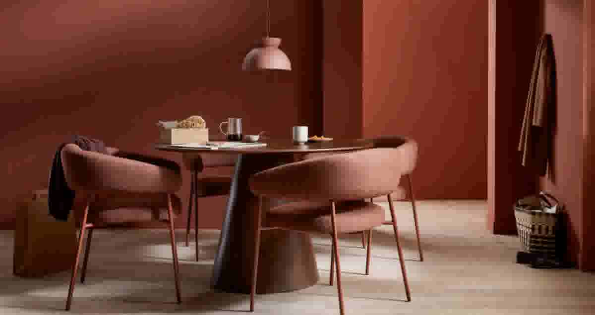 Ronde donkerhouten eettafel met roze stoelen in een terracotta kamer. Hanglamp, brood en koffie op tafel.