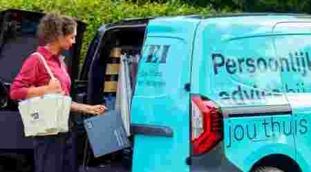 Karwei adviseur laadt raamdecoratie stalen uit een bedrijfsbusje van Karwei met "Persoonlijk advies bij jou thuis" erop. 