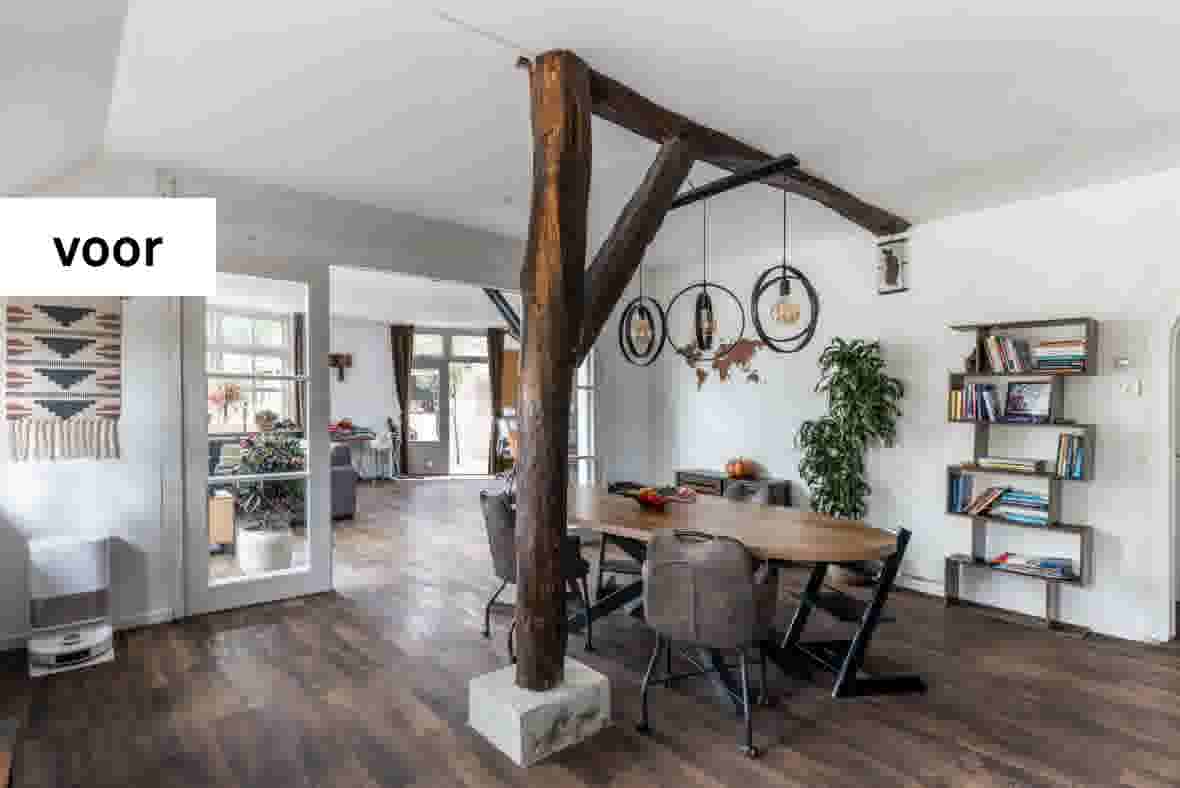 Moderne eetkamer met houten balken, ronde tafel, grijze stoelen, hangende lampen en boekenplanken aan witte muur.