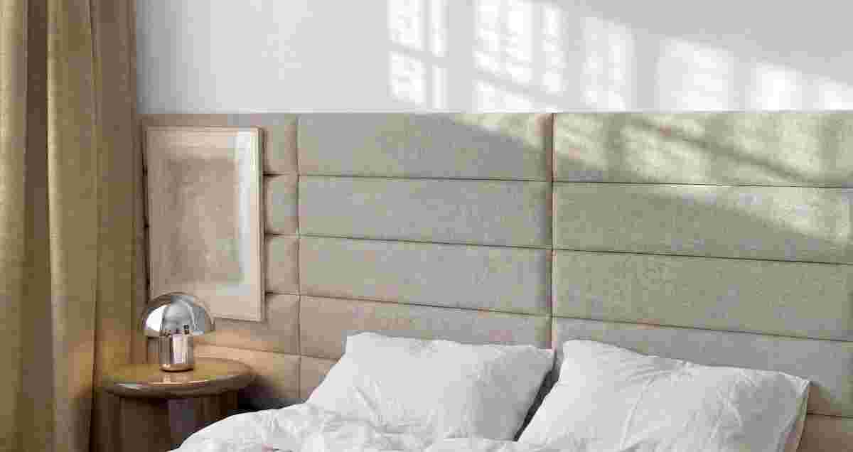 Crème gestoffeerde zitbank met zachte bekleding tegen beige muur, houten tafelblad en gouden wandlamp erboven.