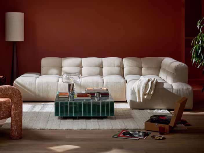 Crème bank voor terracotta muur, met groene salontafel, boeken, lamp en vinylplaten op de vloer.