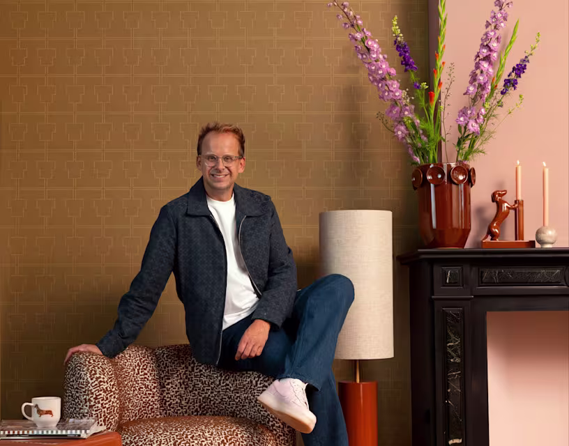 Theo-Bert Pot op een fauteuil voor het oker gele behang uit zijn collectie.