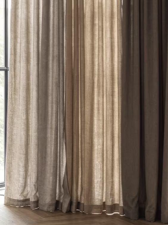 Lange gordijnen in natuurlijke tinten beige, grijs en bruin hangen voor een raam met donkere houten vloer.