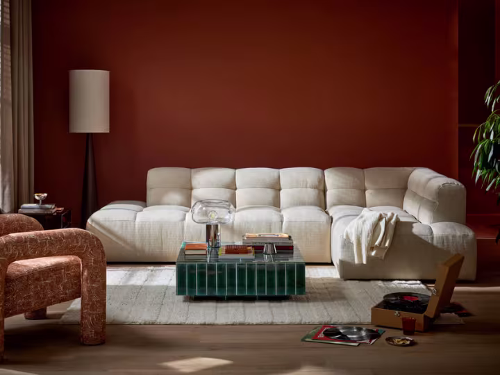 Moderne woonkamer met crèmekleurige bank, terracotta muur, glazen salontafel en staande lamp in een warm interieur.
