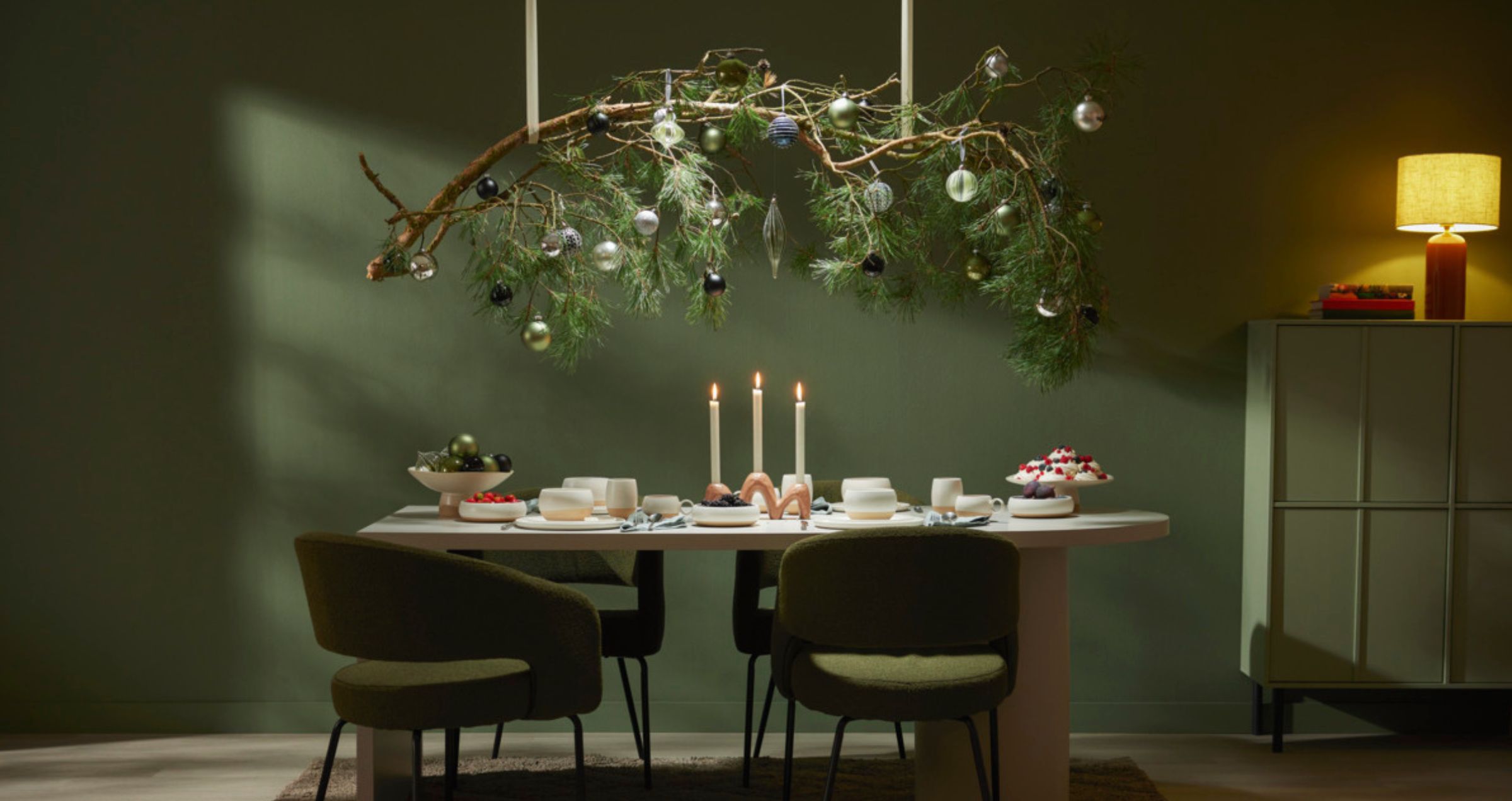 Gedekte tafel met kaarsen en hangende kersttak in groene, sfeervolle kamer