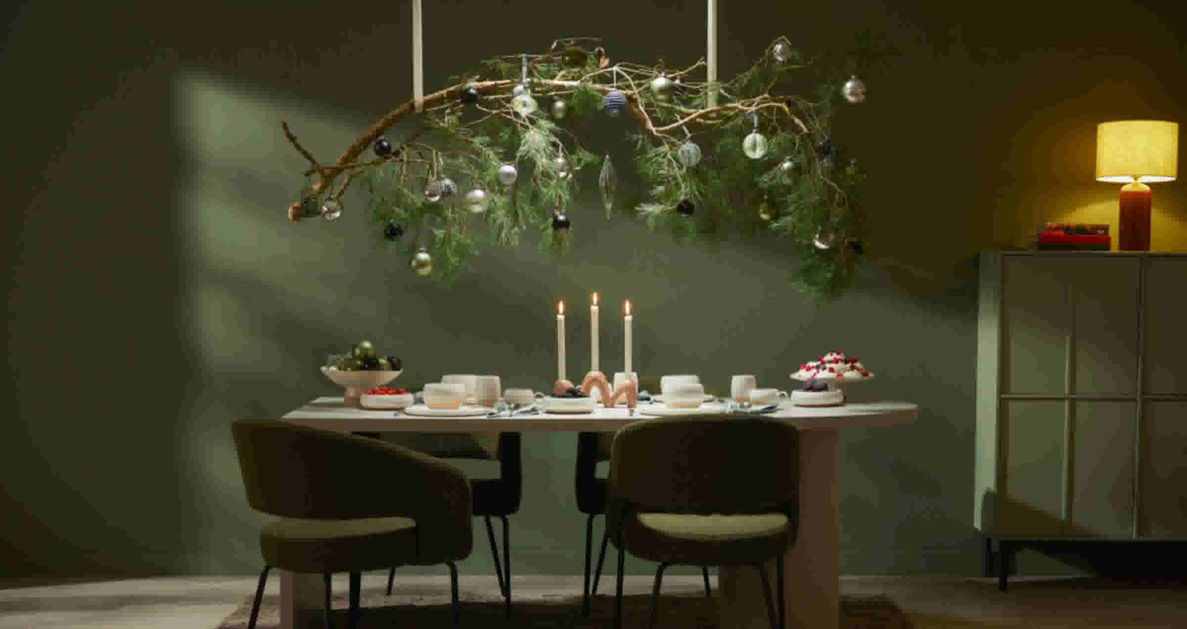 Gedekte tafel met kaarsen en hangende kersttak in groene, sfeervolle kamer