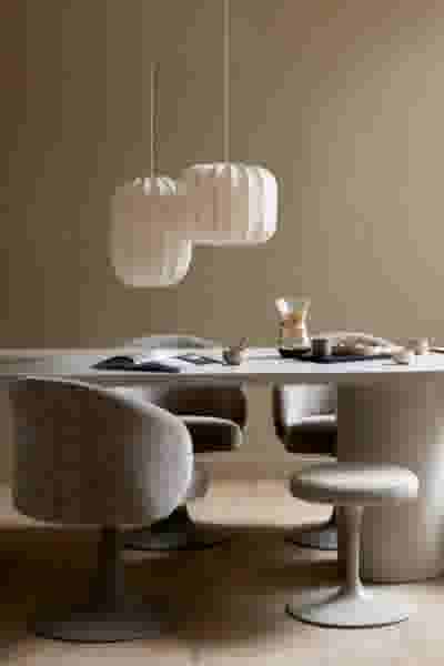 Moderne eetkamer met twee witte hangende lampen, ronde grijze stoelen en een tafel met koffieset en opengeslagen boek.