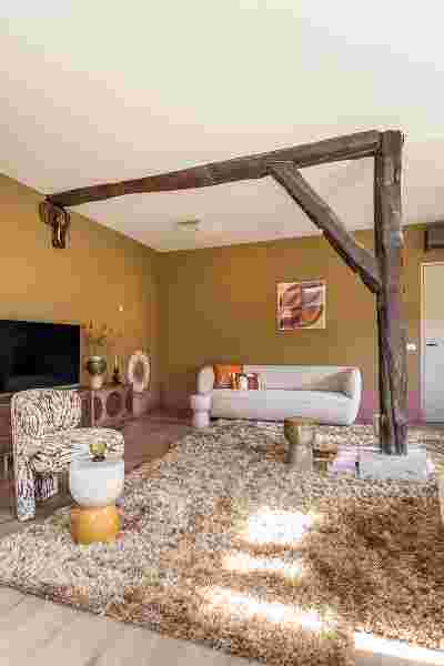 Moderne woonkamer met okerkleurige muren, houten balken aan plafond, pluizig tapijt en crèmekleurige meubels.