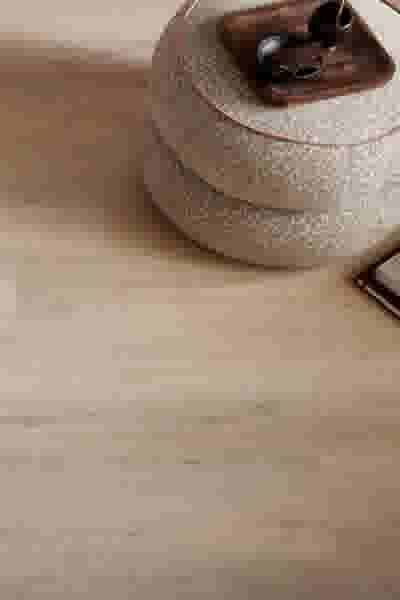 Ronde beige poef met gespikkeld patroon op lichte houten vloer, met kleine houten dienblad en accessoires erop.